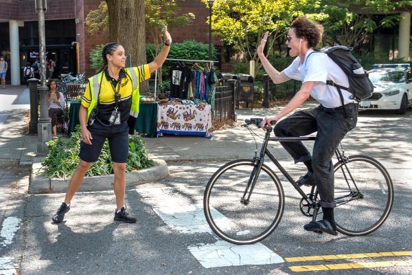 A cyclist hi-fives a cross guard as they bike past the pedestrian crossing in front of the student commons.